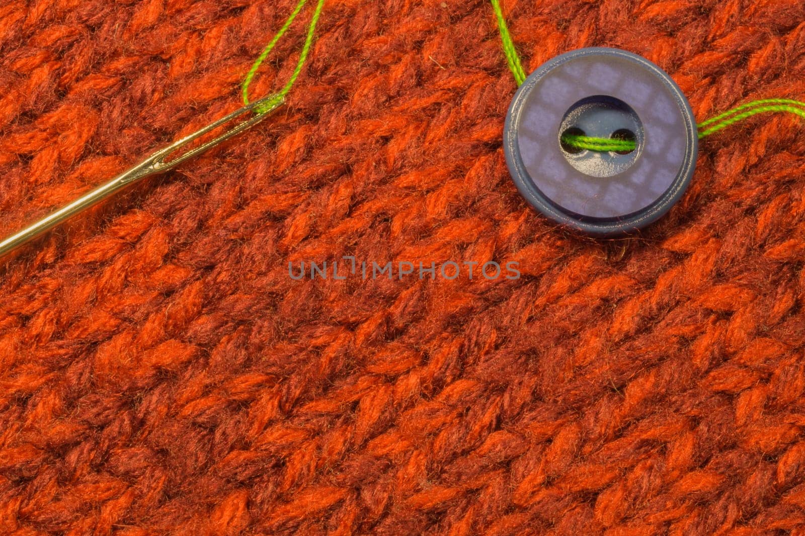 Button and needle with thread on red textile background