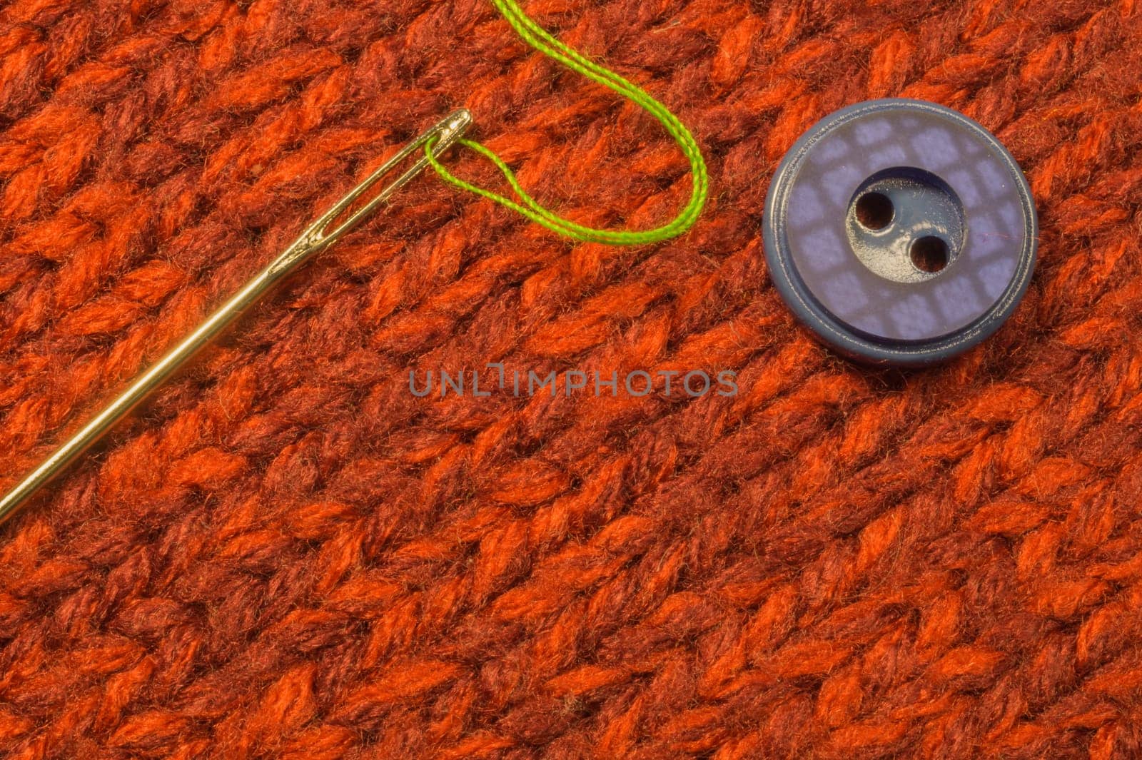 Button and needle with thread on red textile background