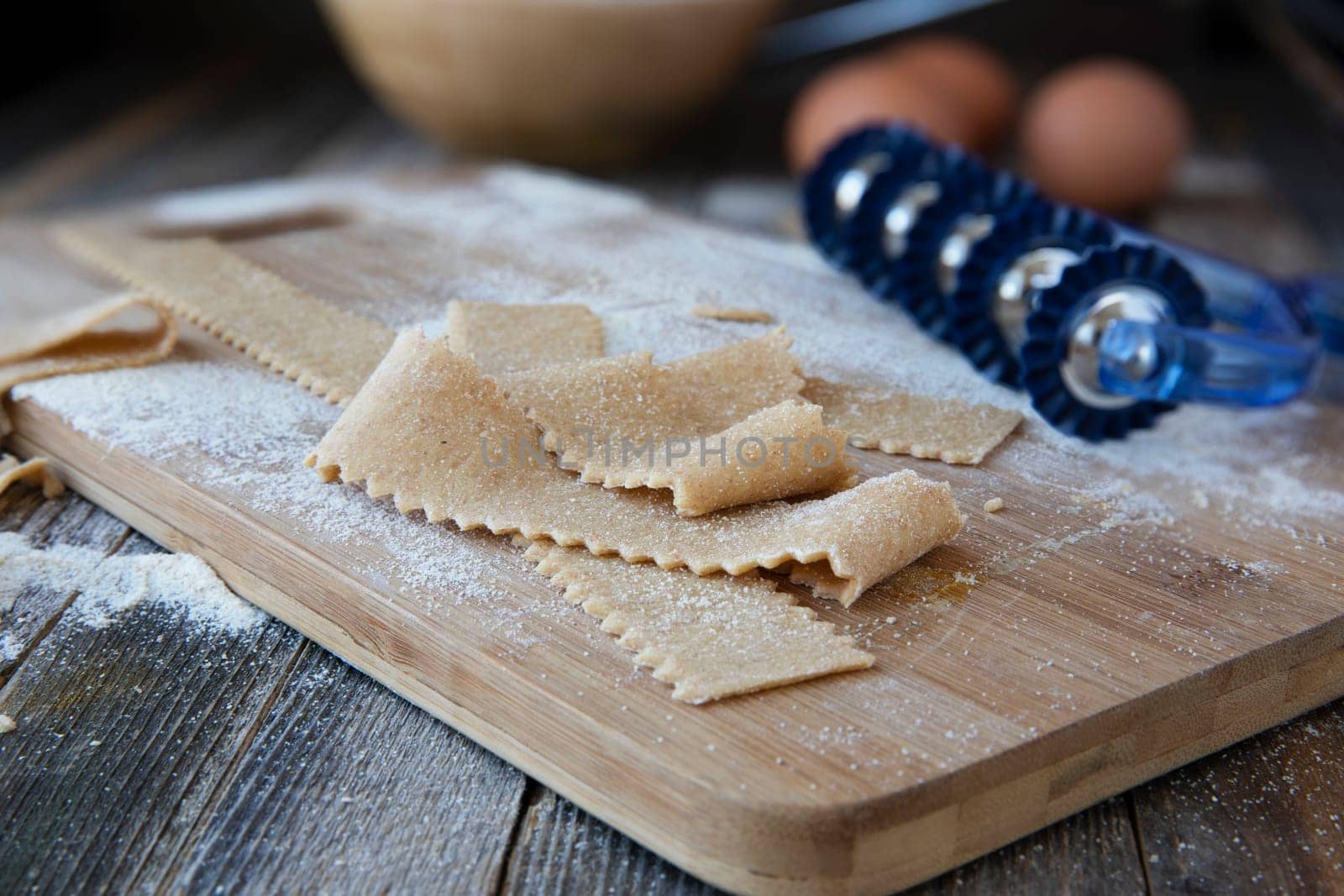 Fresh cut homemade pappardelle pasta on wooden board with cutter.