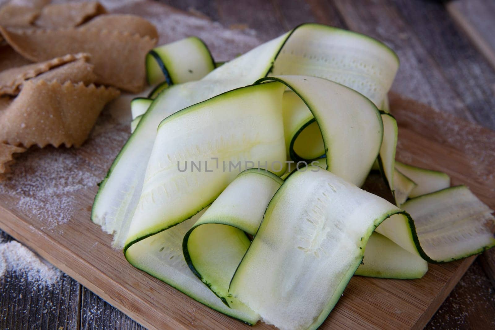 Fresh cut zucchini ribbons on cutting board with homemade pappardell pasta in background.
