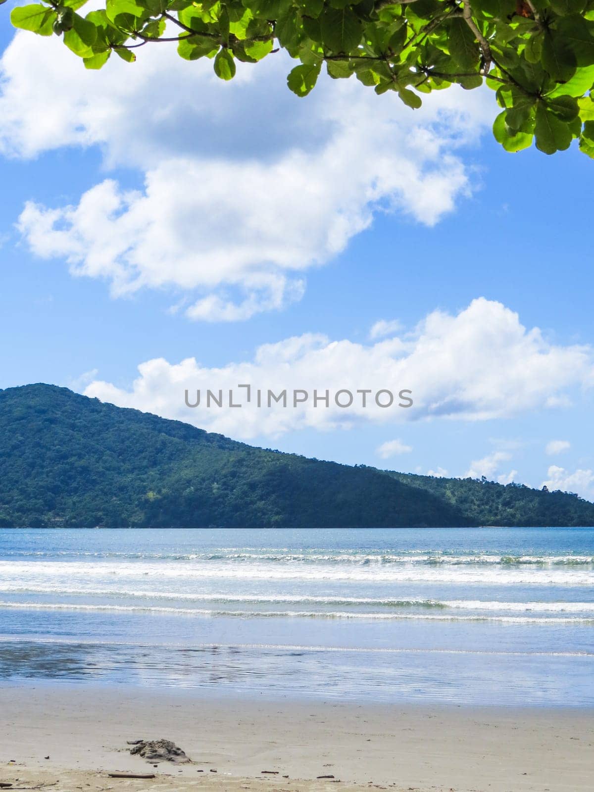 View of quiet beach in sunny day with blue sea and island in the background.