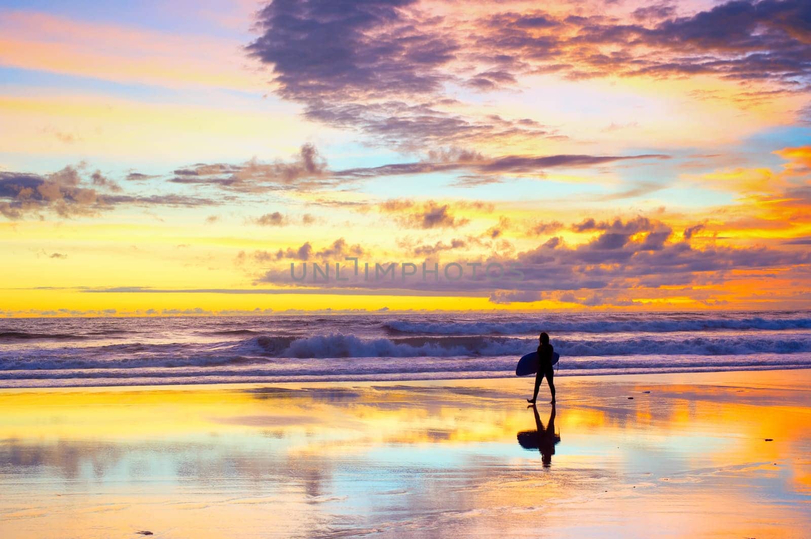 Silhouette of surfer walking by the beach with surfboard at sunset. Bali, Indonesia