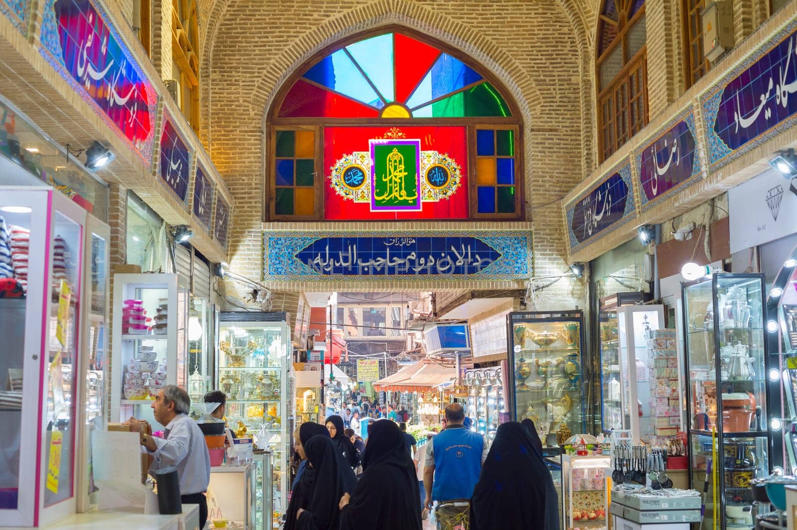 TEHRAN, IRAN - MAY 22, 2017: Crowd of people in row of Grand Bazaar with stalls of dishes. Interior of Grand Bazaar