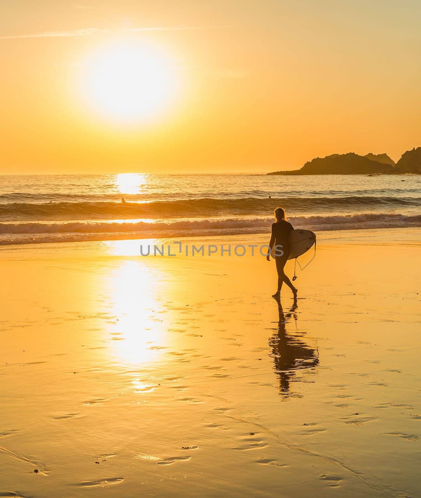 Silhouette of surfer walking to the ocean by sandy beach, scenic golden sunset over seascape, Sagres, Algarve, Portugal