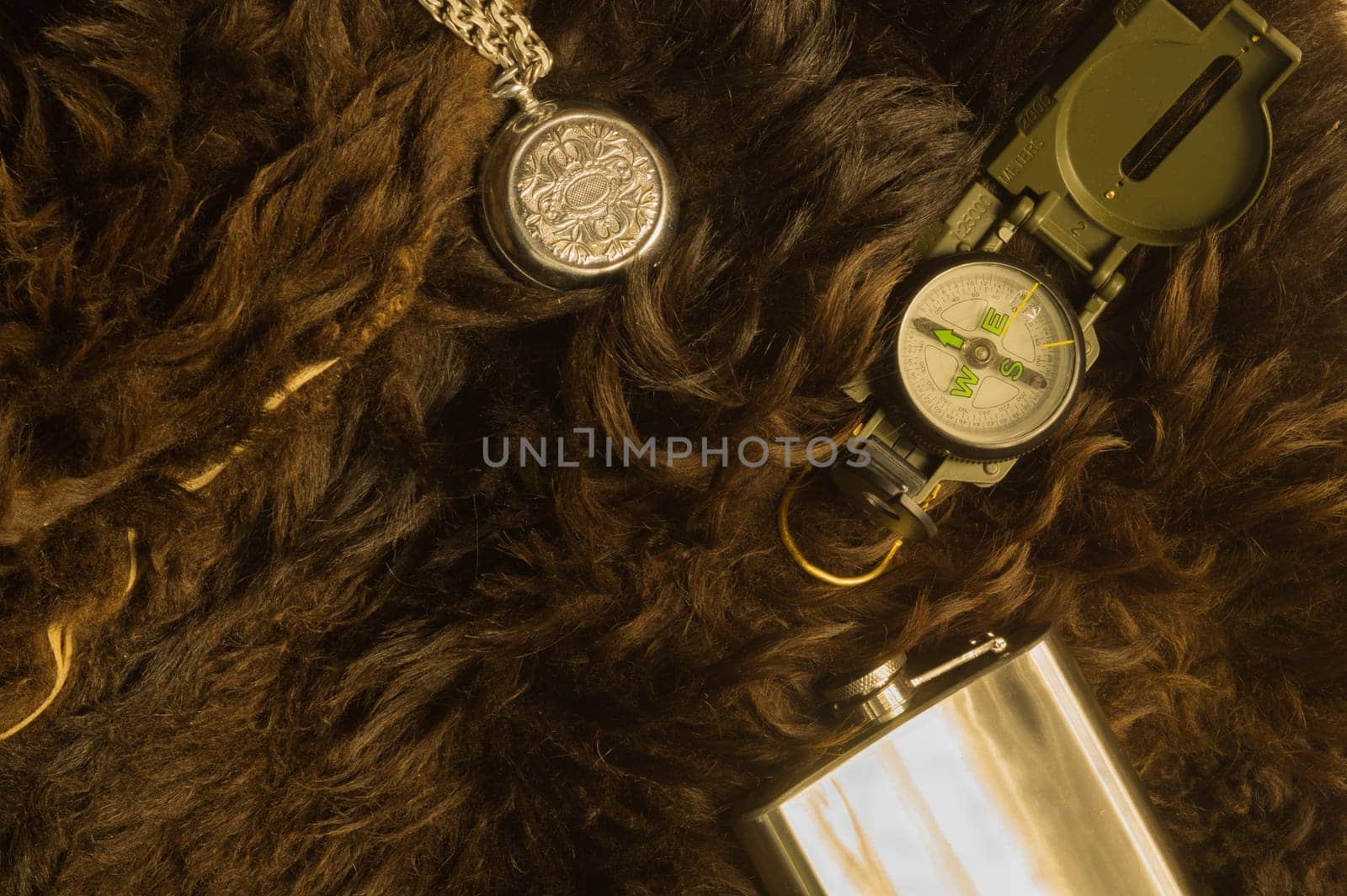Old steel clock with the compass and the flask on the fur background