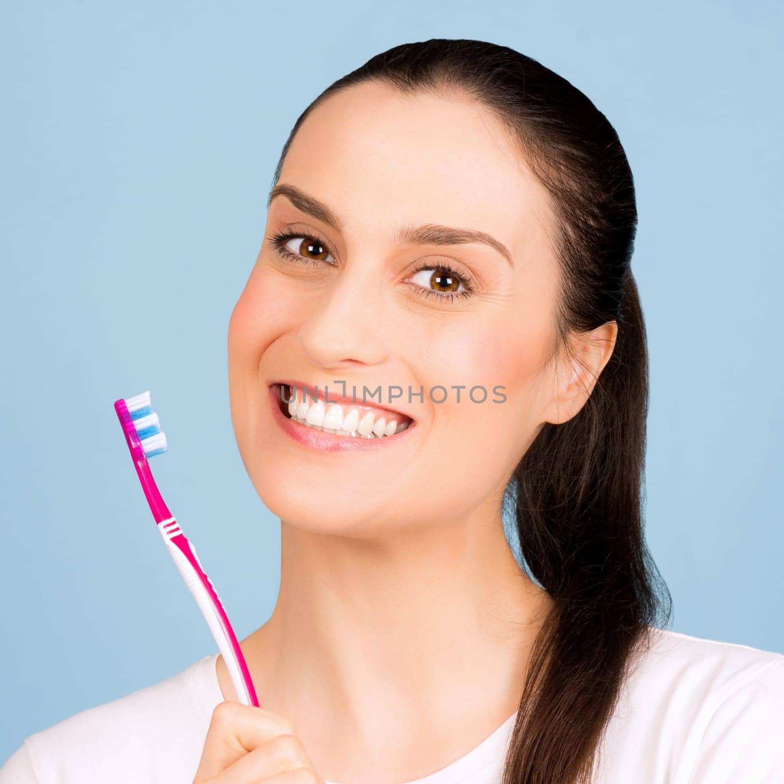 Beautiful smiling woman with white healthy teeth is holding a toothbrush on blue background, oral hygiene concept.