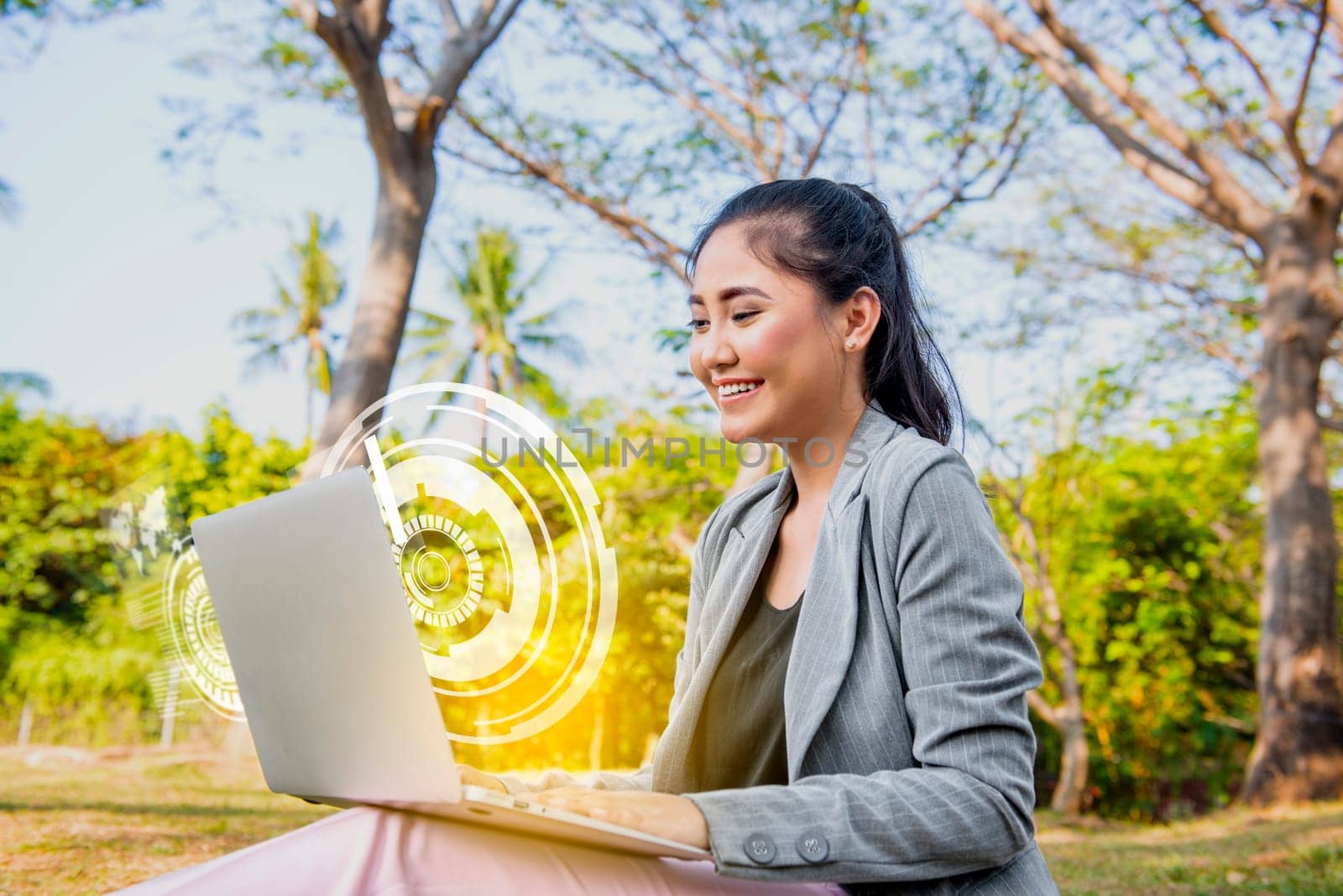Smiling asian business woman looking at the laptop with virtual screen which display the interface of world maps and binary code on the park. Digital technology concept