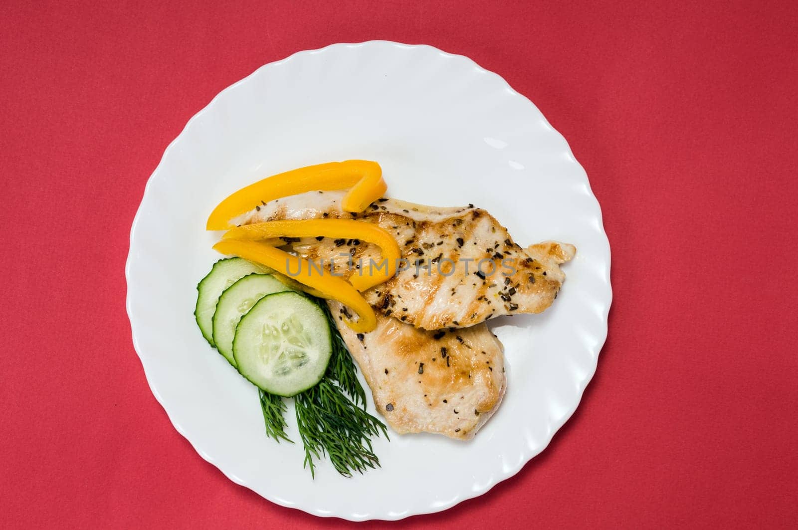 grilled chicken fillet on a white plate and red background