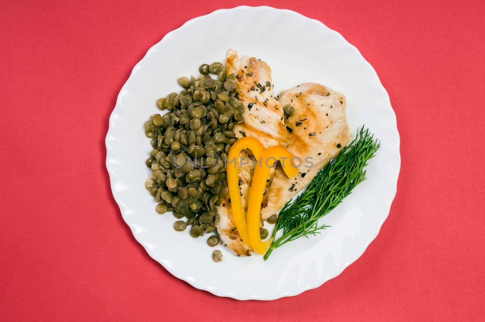 grilled chicken fillet with lentils on a white plate and red background
