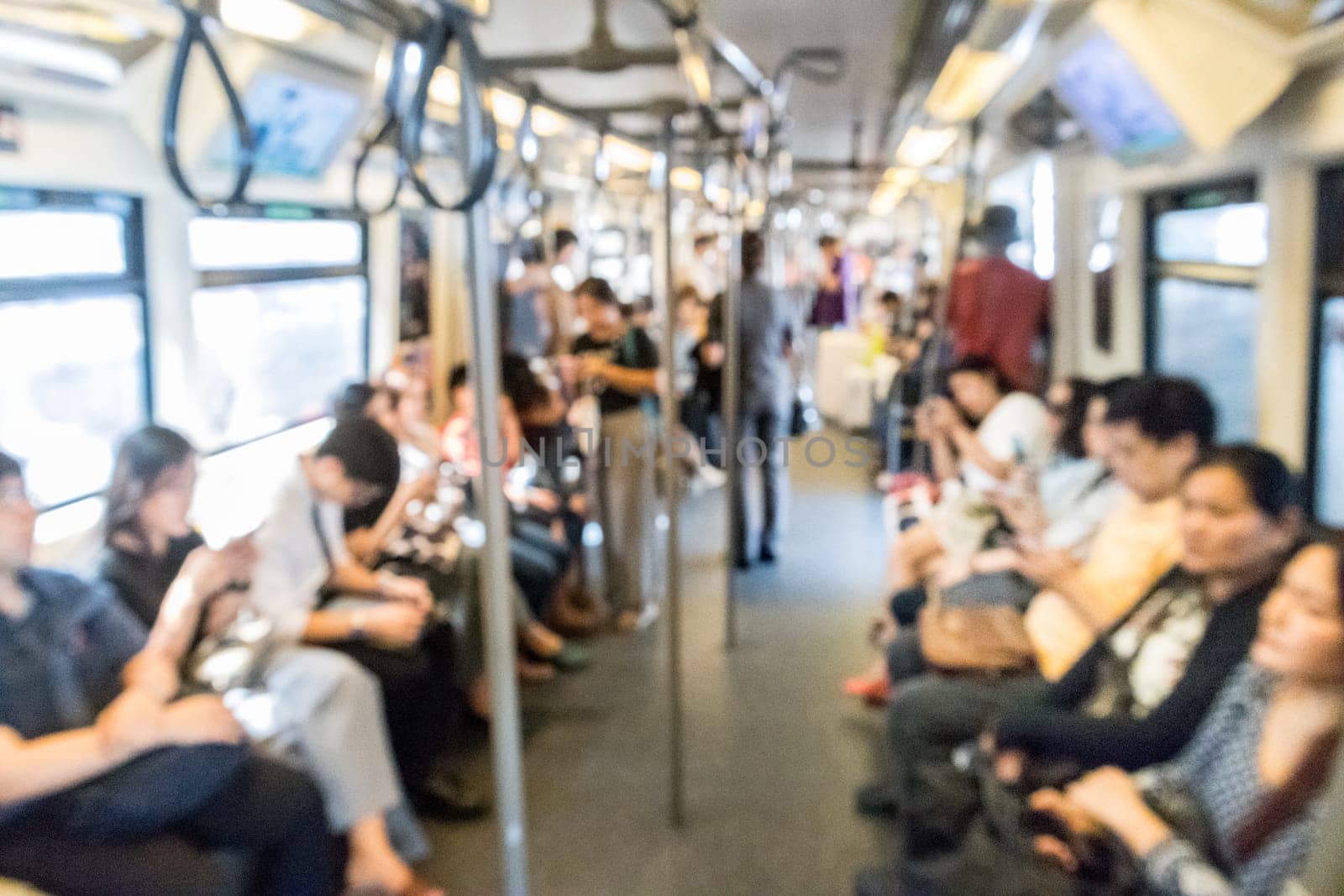 Blured image of unrecognizable asian people using their mobile phone devices while commuting by city subway in SE Asia.