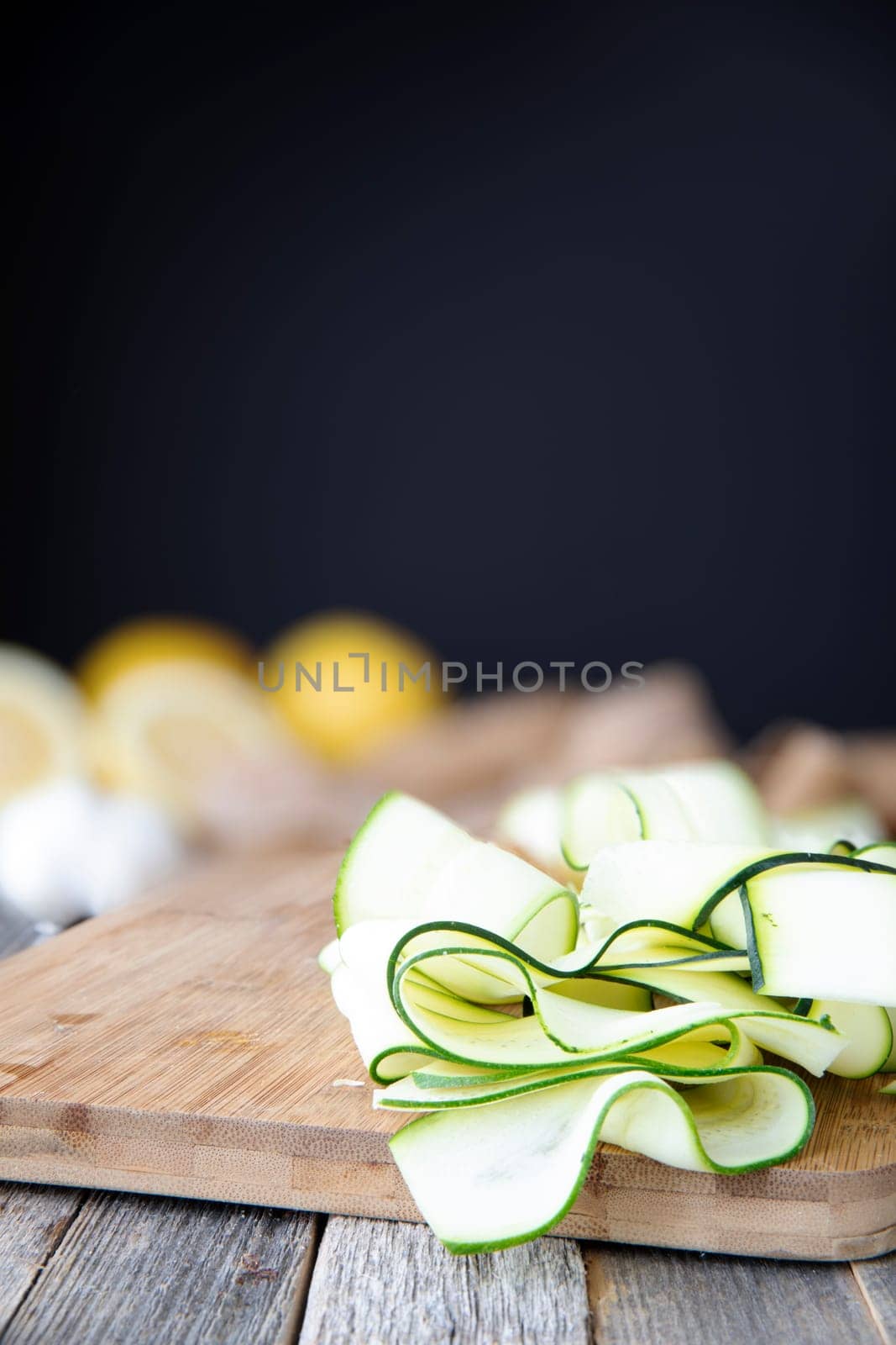 Fresh zucchini sliced into ribbons and sitting on wooden cutting board with copy space at top.