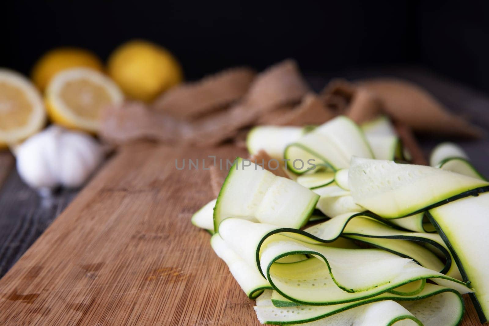 Fresh zucchini sliced into ribbons and sitting on wooden cutting board.