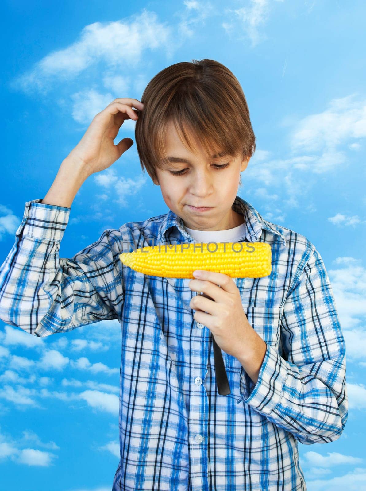 Young farm Boy holding a boiled corn on a background of blue sky