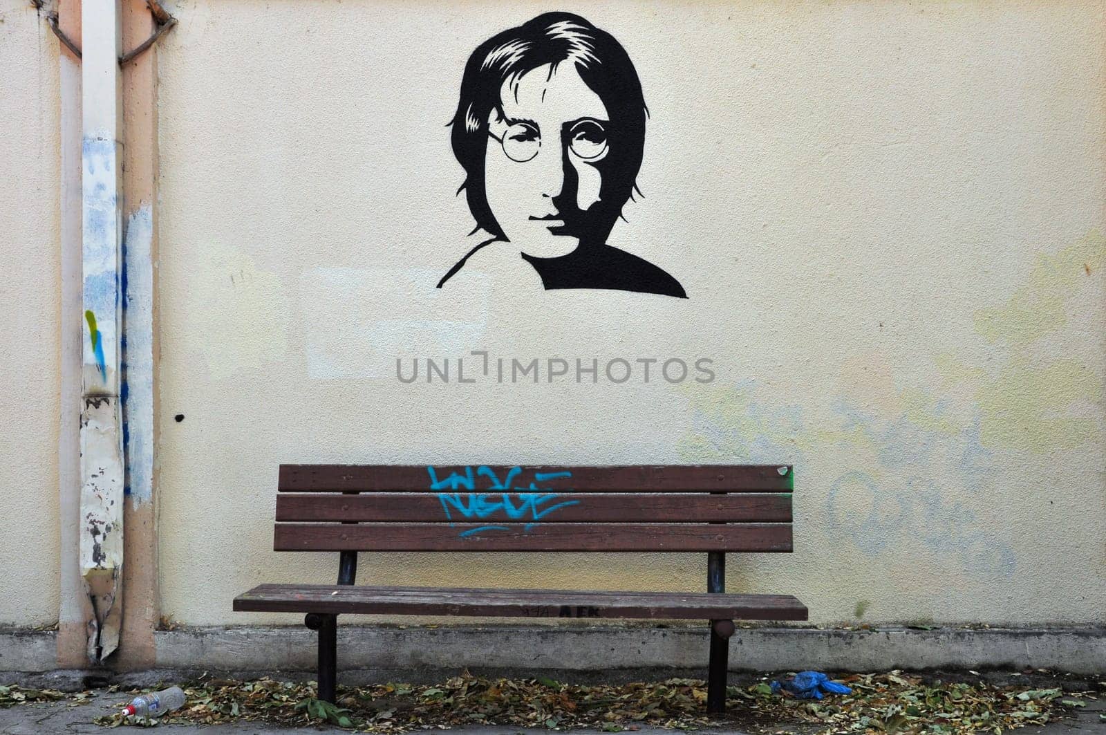 ATHENS, GREECE - AUGUST 30, 2014: Famous musician John Lennon from The Beatles portrait stencil graffiti on textured wall and wooden bench.
