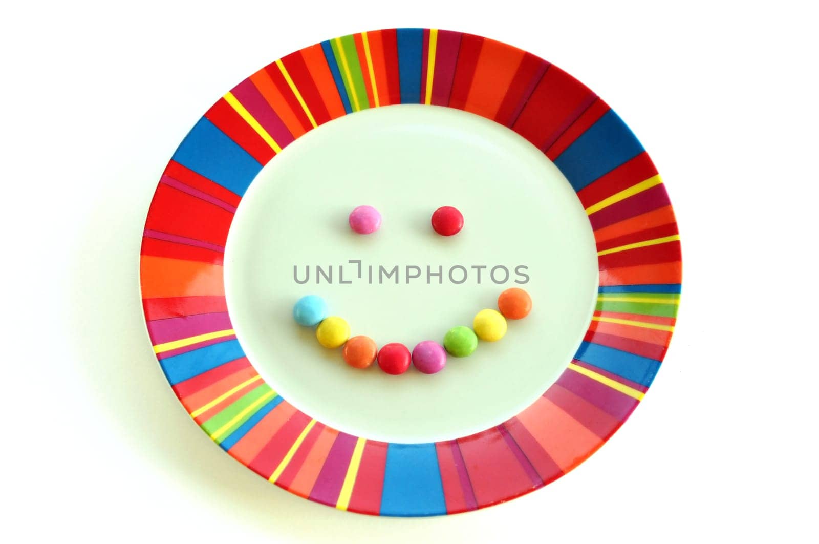 Smiling face made from candy and colorful plate on white background. Kids dessert food happy meal.