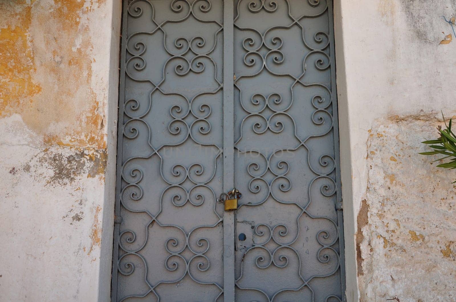 Iron gate with old fashioned metalwork pattern and textured wall background. Abandoned house exterior.