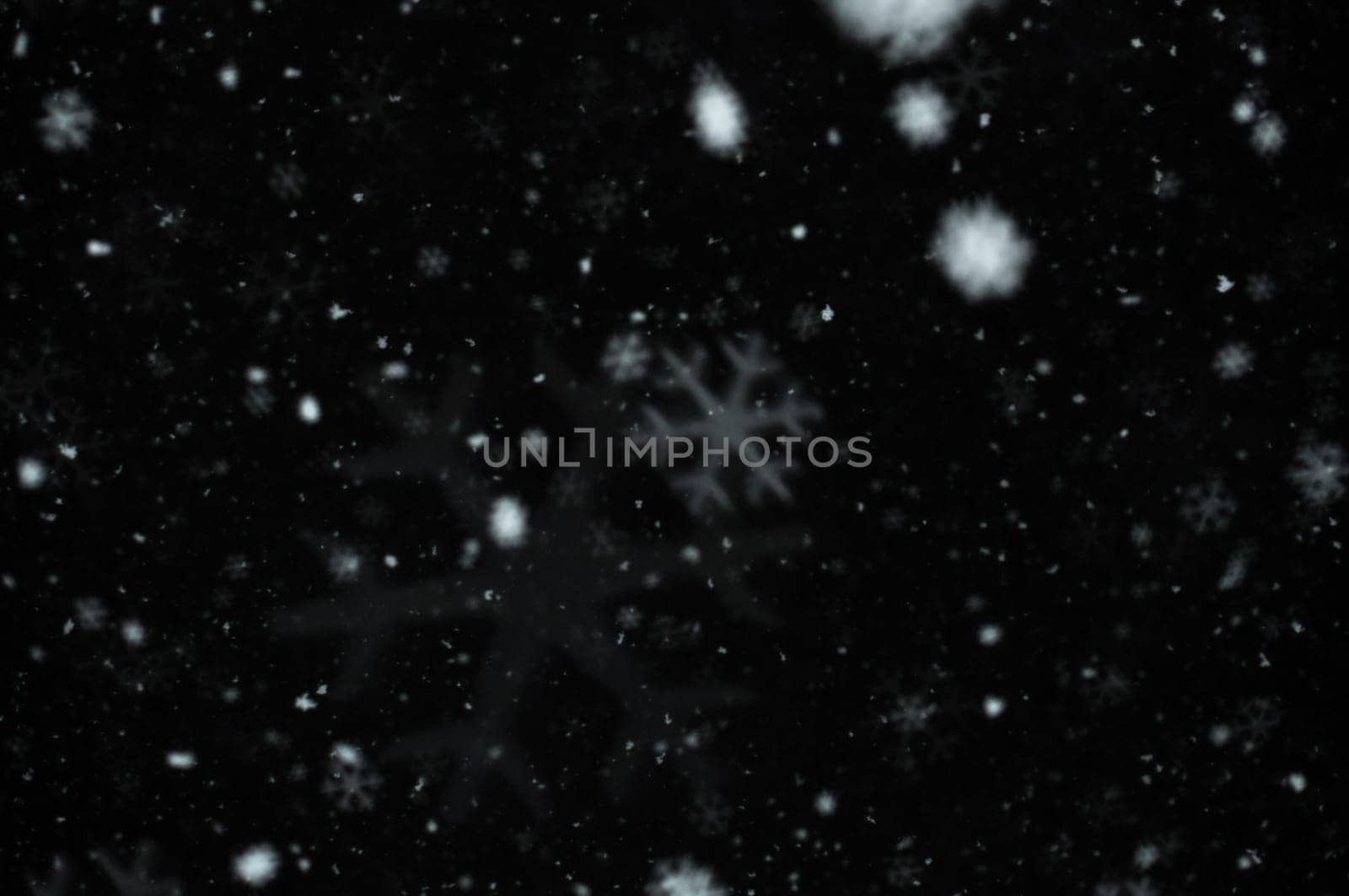 Snow falling on dark winter night. Snowflakes bokeh effect abstract blur.