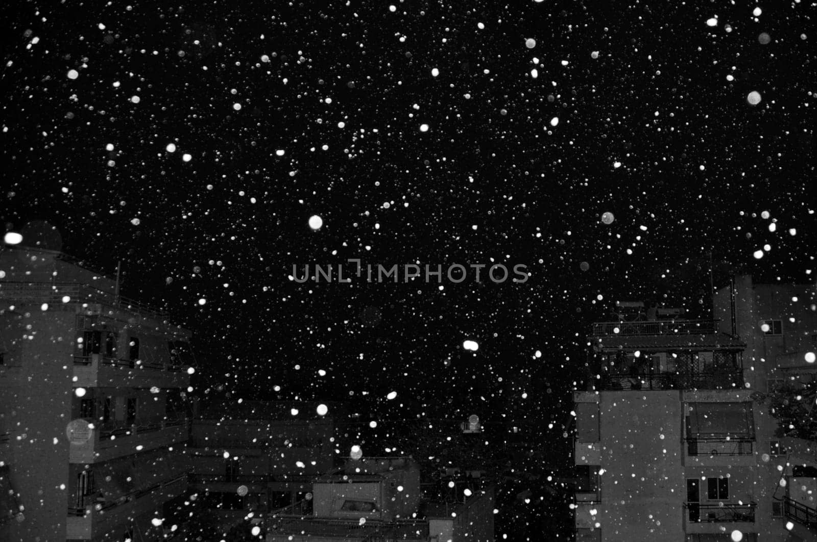 Snow falling over city buildings at night. Black and white.