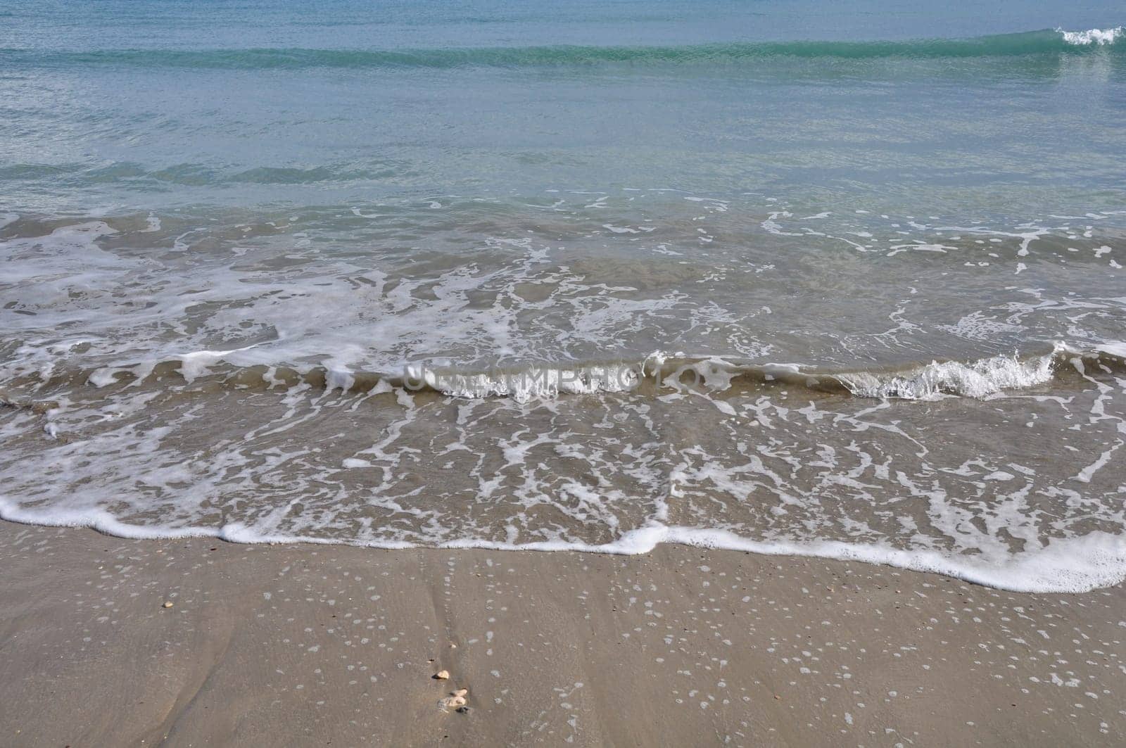 Waves crashing on sandy beach. Waters edge abstract sea background.