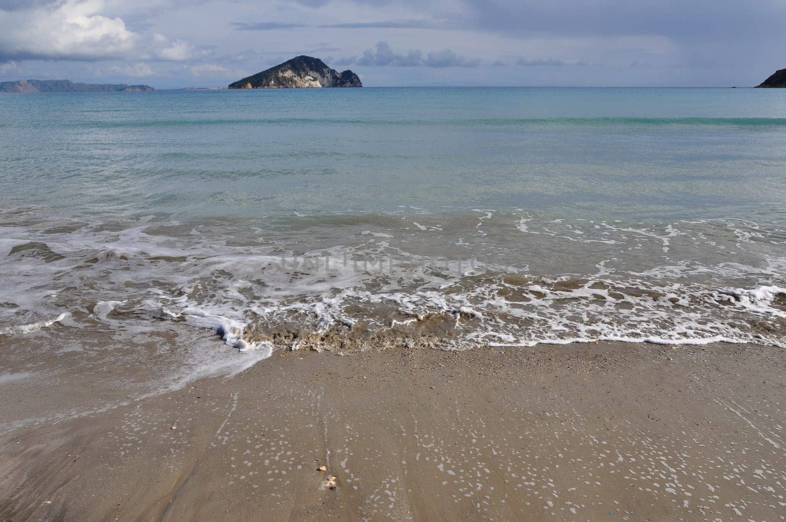 Waves splashing on sandy beach Keri in Zakynthos Greece and Marathonisi island natural habitat of the caretta-caretta sea turtle.