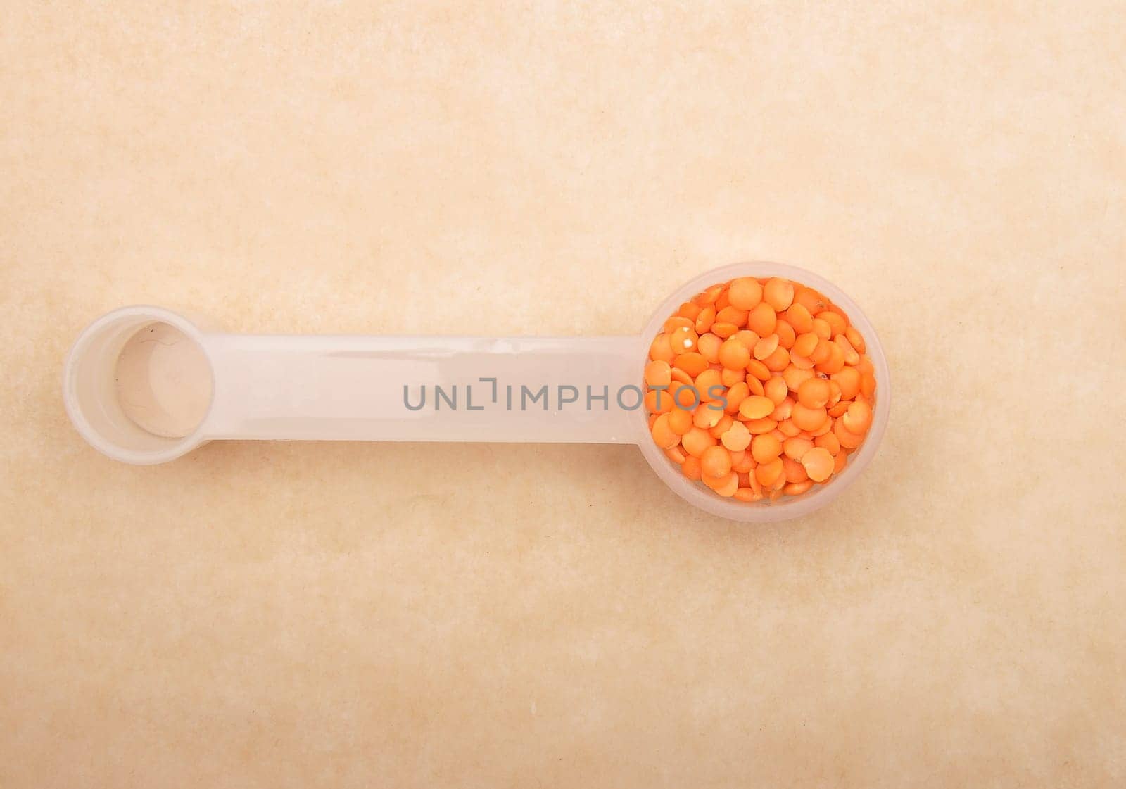Red lentils on measuring spoon and brown background