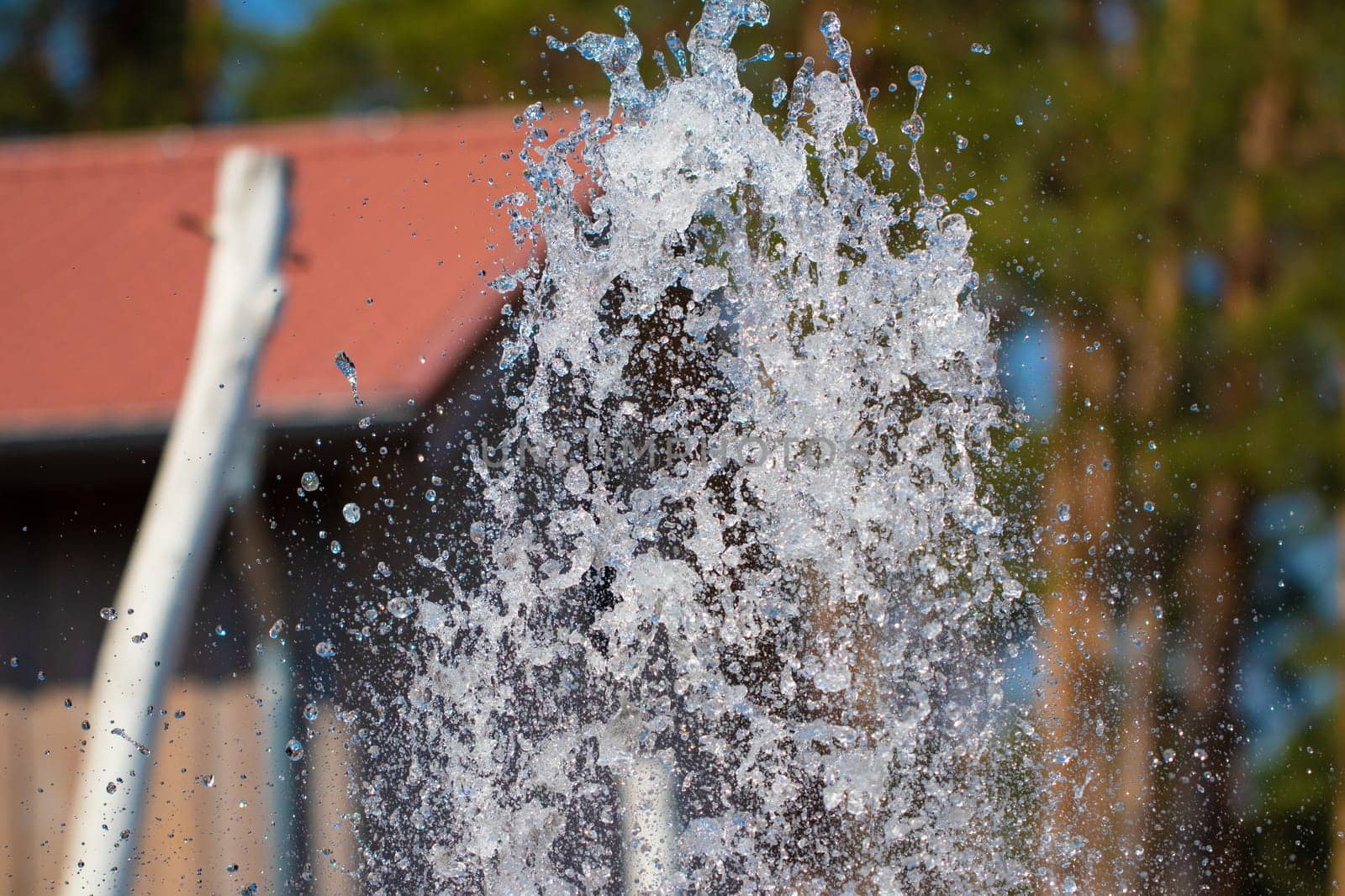 Closeup water. Close-up of the jet of water from a fountain made from natural stones against a blurred light natural background. View of a fountain where droplets scattering in the different sides.