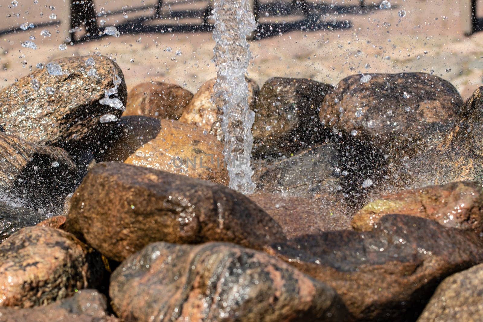 Closeup water. Close-up of the jet of water from a fountain made from natural stones against a blurred light background. View of a fountain where droplets scattering in the different sides.