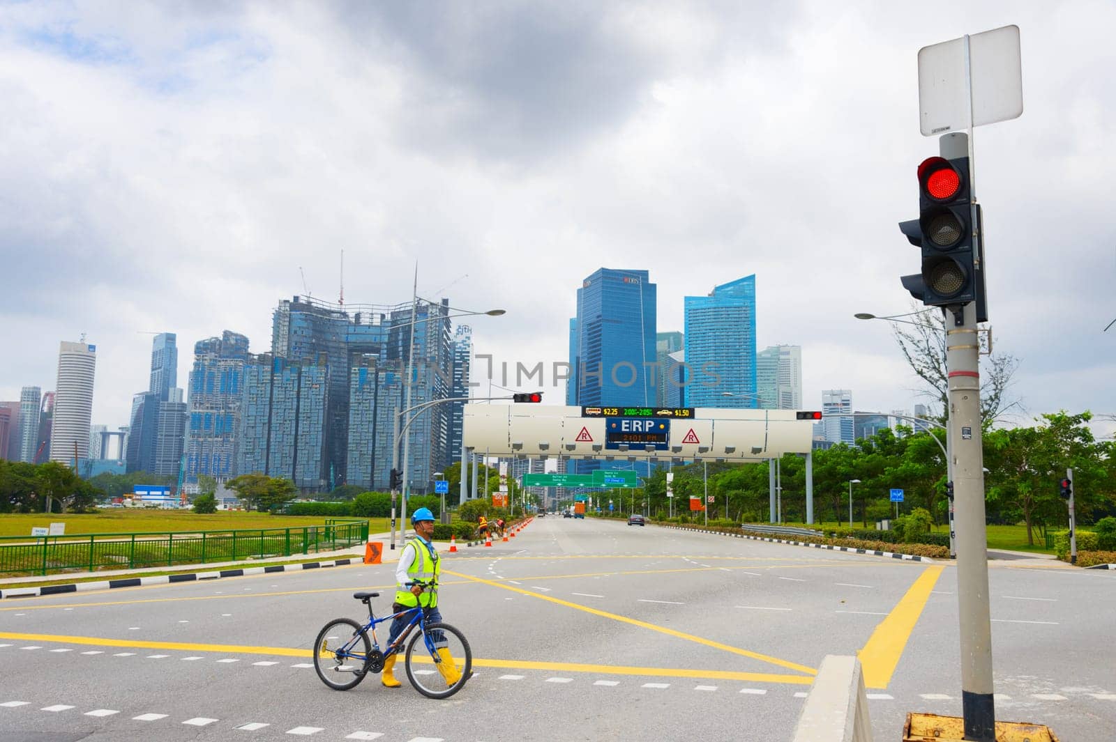 SINGAPORE - FEBTUARY 16, 2017: Construction site worker in helmet and vest crossing road with bicycle, Singapore downtown skyline in background
