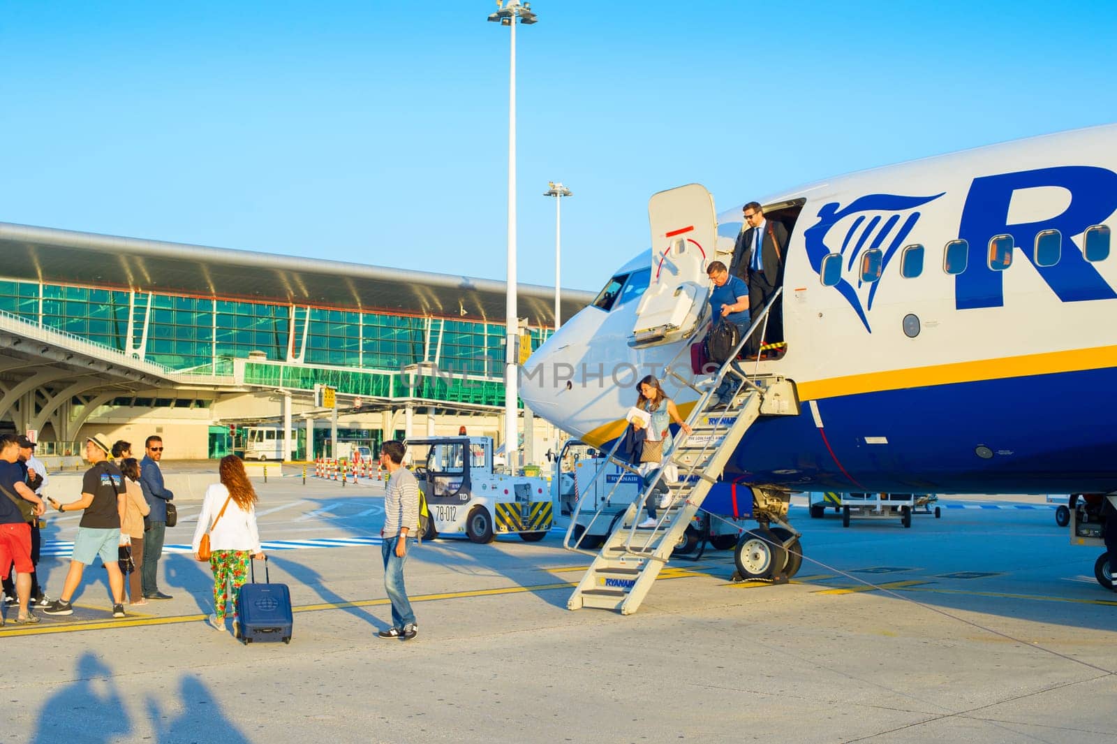 PORTO, PORTUGAL - MAY 24, 2017: Passengers leaving airplane by ladder, glass facade of airport in background