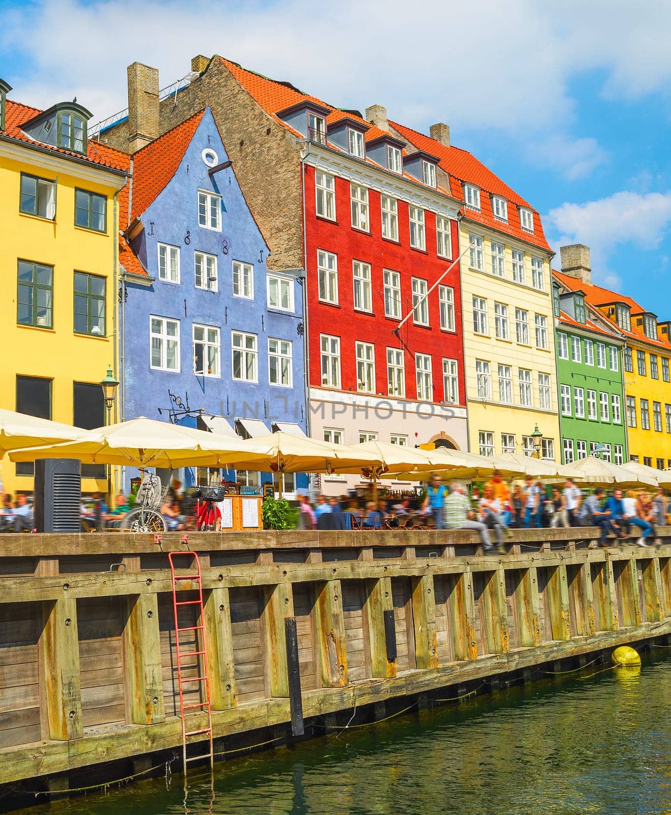 Old town with Nyhavn harbor view in bright sunny day, tourists walking and sitting in bars, cafes, restaurants by canal, Copenhagen, Denmark
