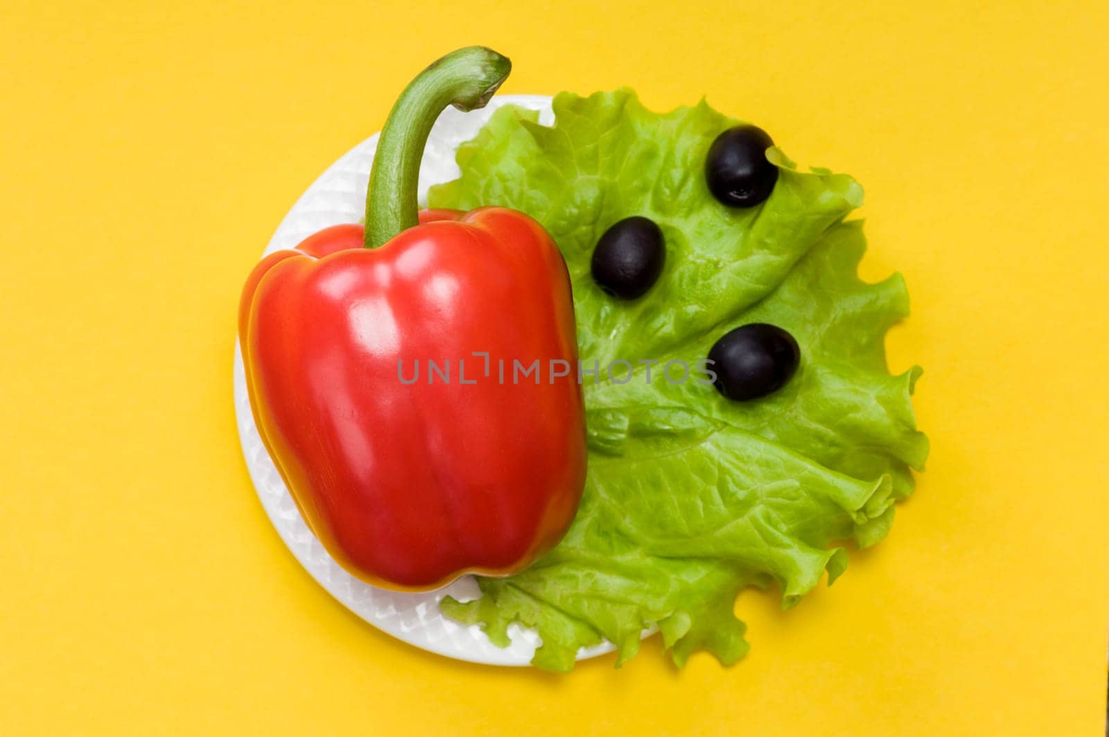 Bell pepper, olives, salad lettuce on white plate on yellow background