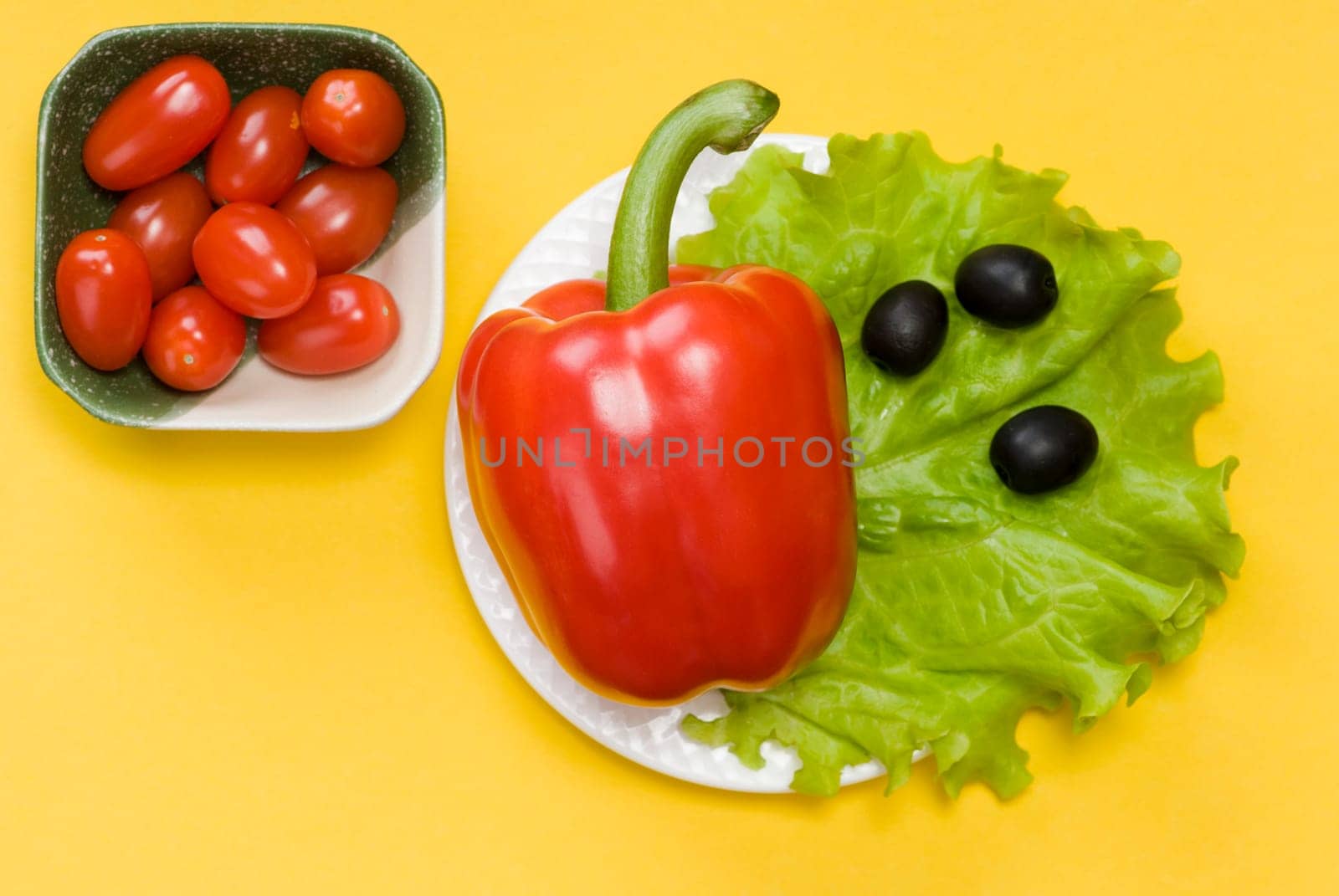 still life of bell pepper, tomato cherry, lettuce and olives on yellow background