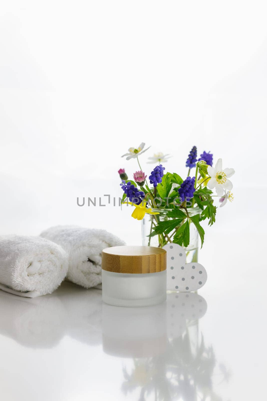 Towels next to a cream jar in front of white background and flowers in a vase.