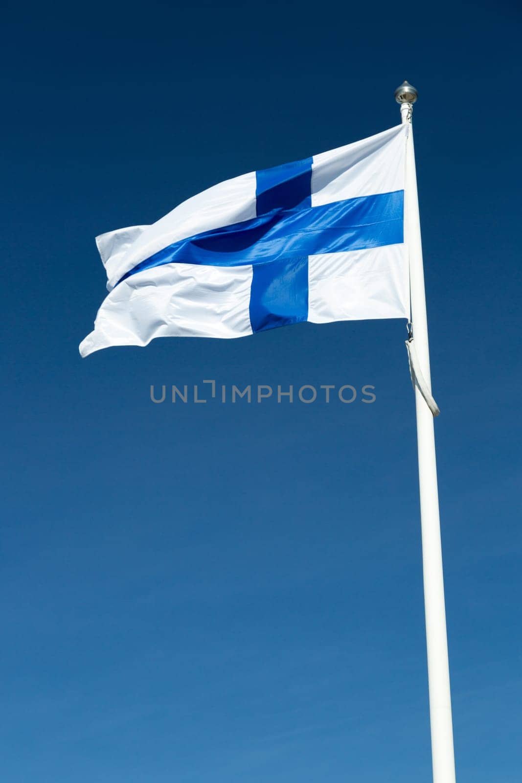 The Finnish Flag on a Flagpole waving in the wind with a blue sky.