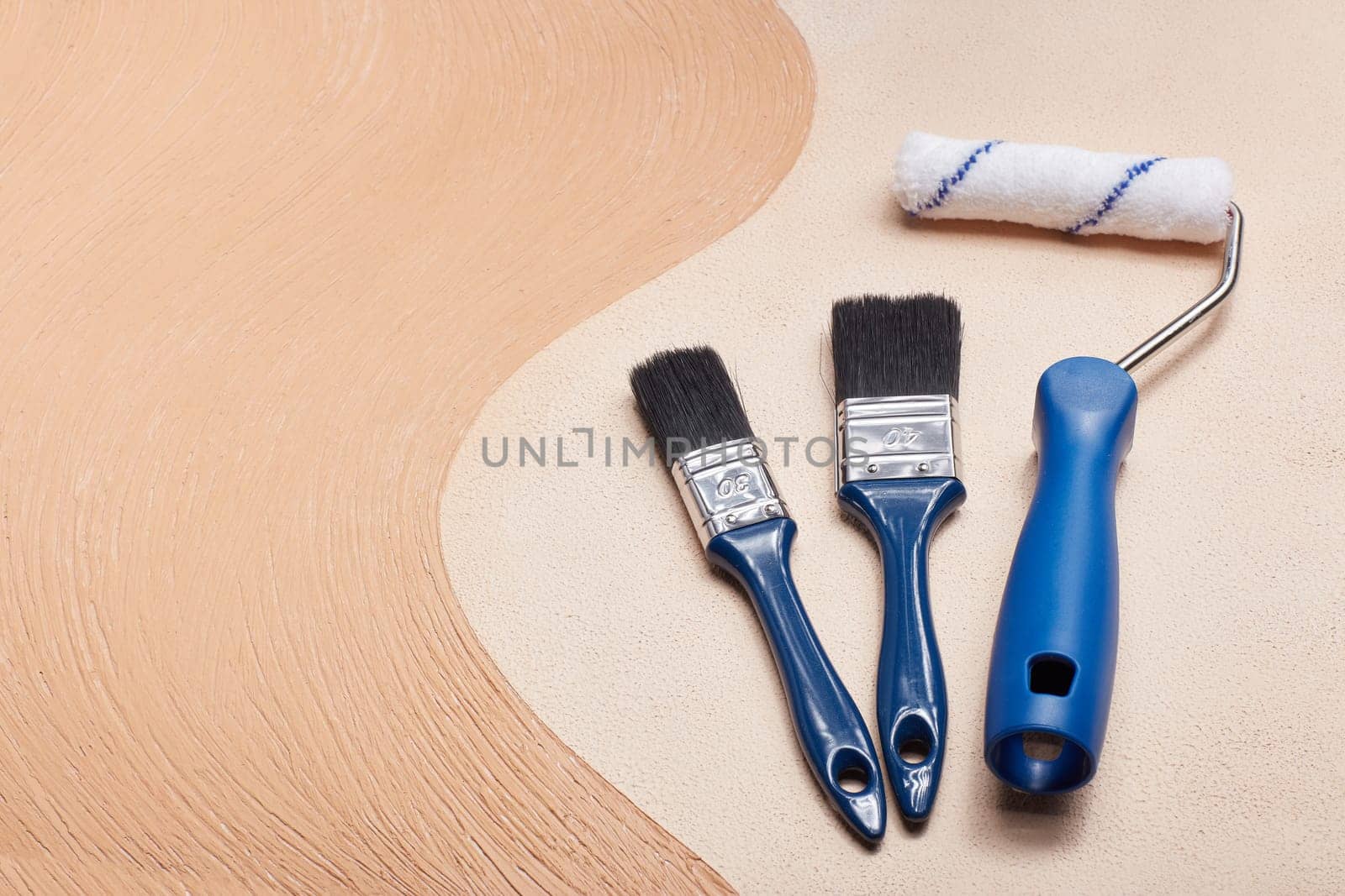 Blue paint brushes and roller lying on textural double background consisting of two beige shades. Top view with copy space, Concept of construction or design office