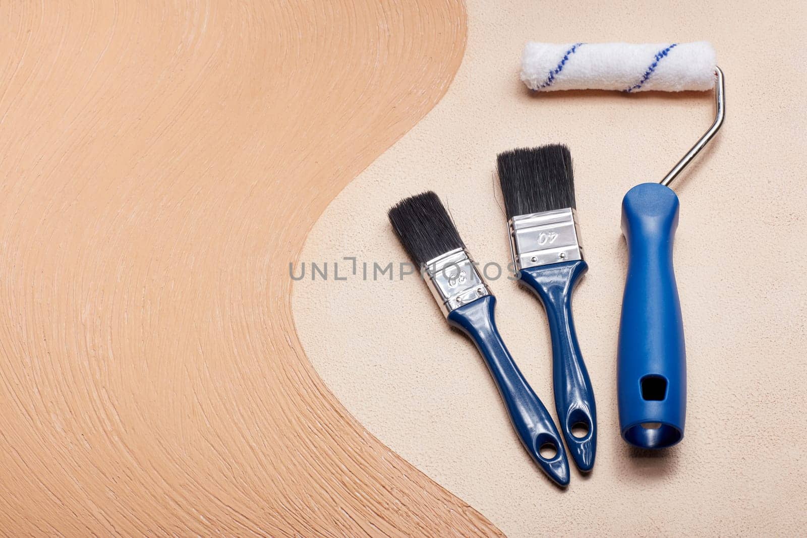 Blue paint brushes and roller lying on textural double background consisting of two beige shades. Top view with copy space, Concept of construction or design office