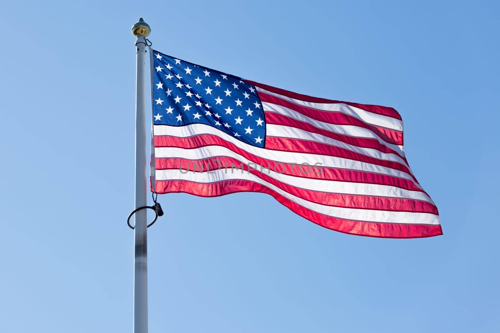 The Flag of the United States of America waving in the wind with a  clear blue sky.