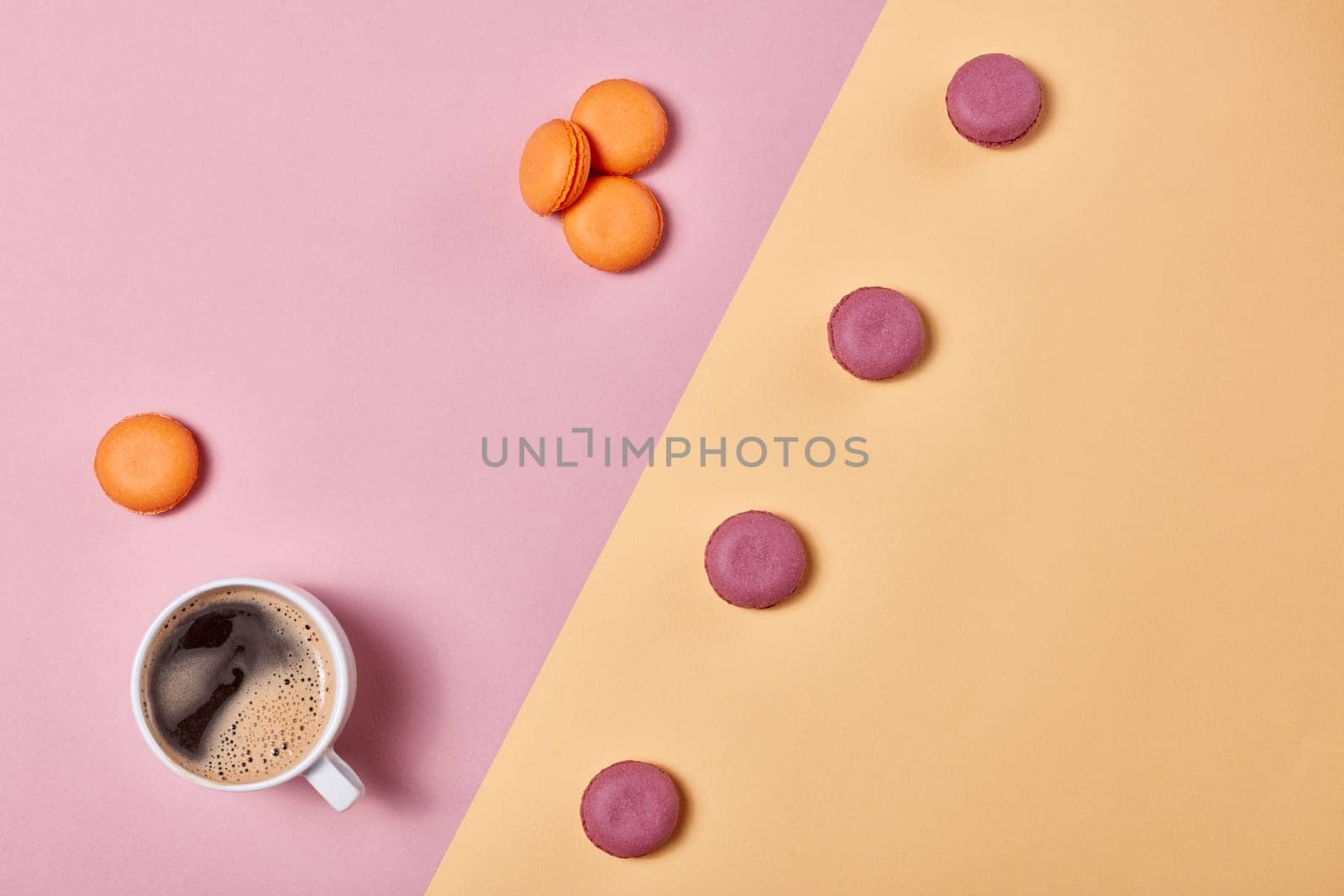 Still life with cup of coffee and delicious macaroons lying on background consisting of two colores pink and yellow. Top view with copy space. Design element for menu of cafe