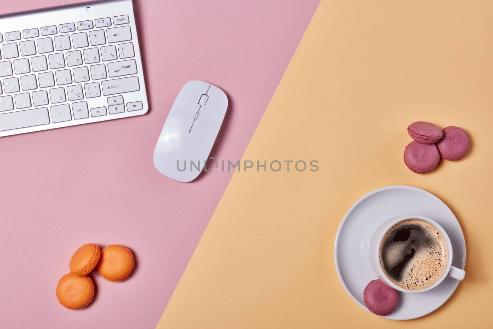 Cup of coffee, macaroons, computer keyboard and mouse on background consisting of two colores pink and yellow. Top view with copy space. Design element for menu of cafe, internet cafe, web, workplace.