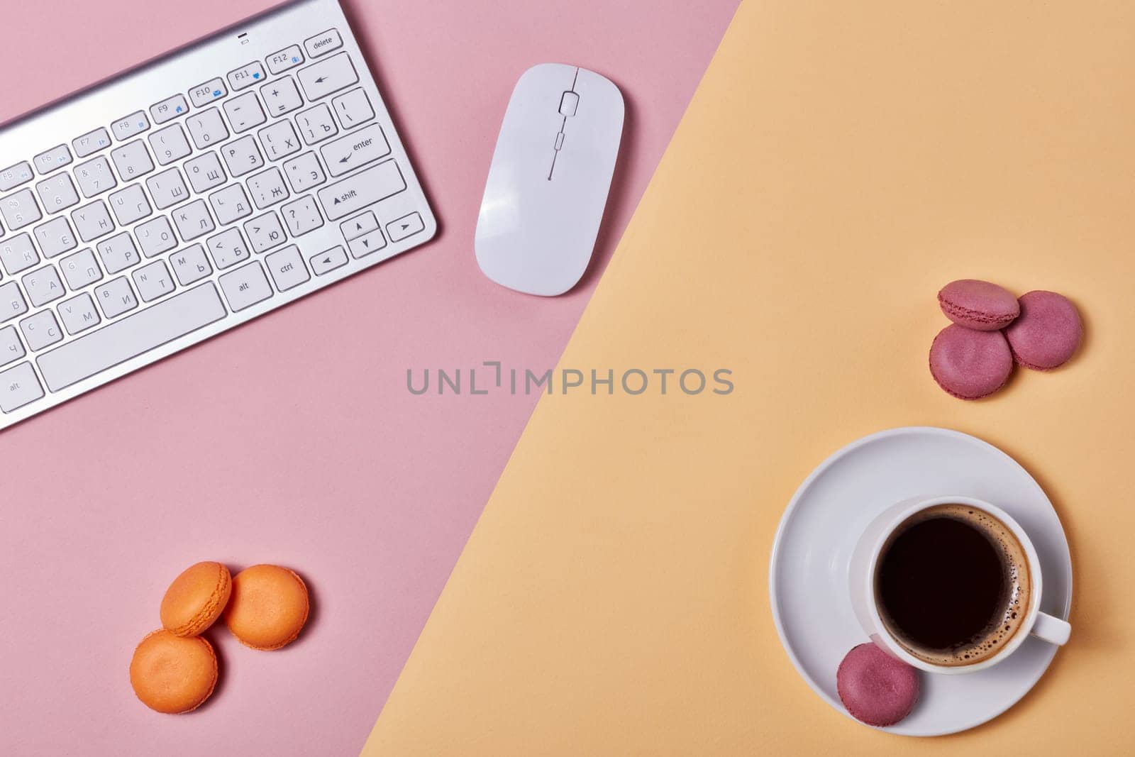 Cup of coffee, macaroons, computer keyboard and mouse on background consisting of two colores pink and yellow. Top view with copy space. Design element for menu of cafe, internet cafe, web, workplace.