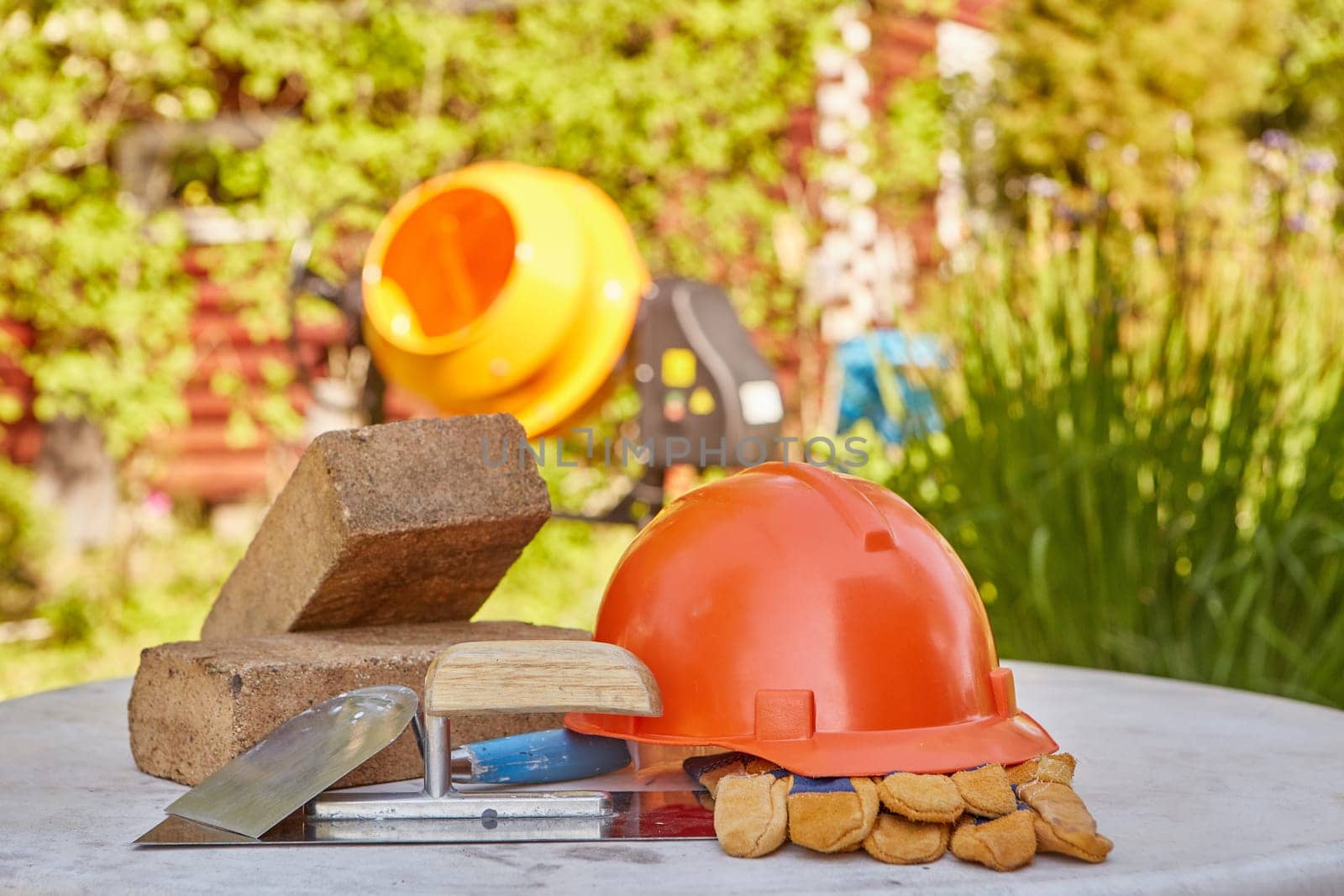 Construction concept. Bricks, tools, hard hat, gloves and concrete mixer. Outdoors