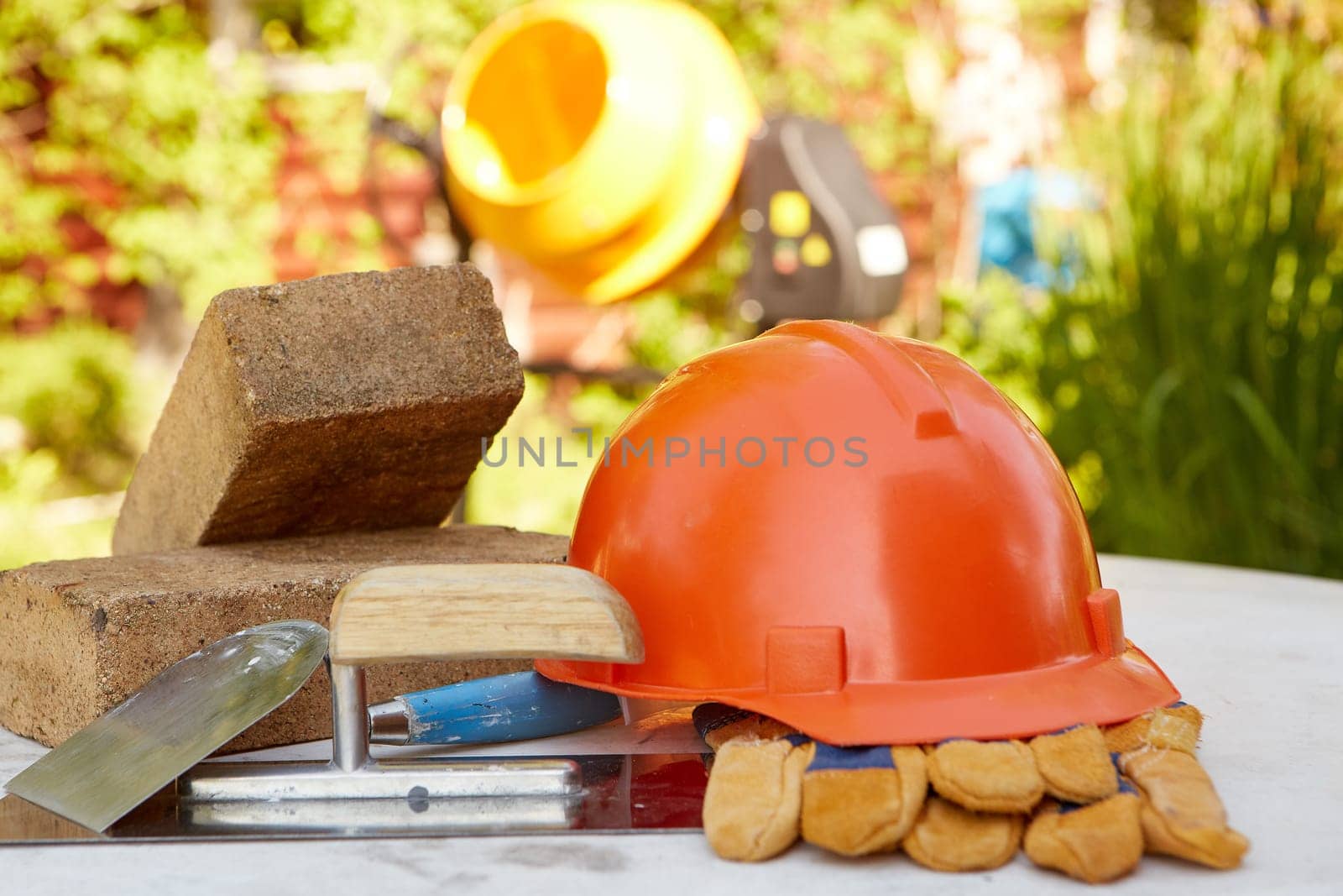 Construction concept. Bricks, tools, hard hat, gloves and concrete mixer. Outdoors