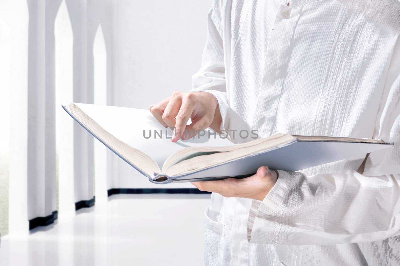 Muslim man standing while reading the quran on his hands in the mosque