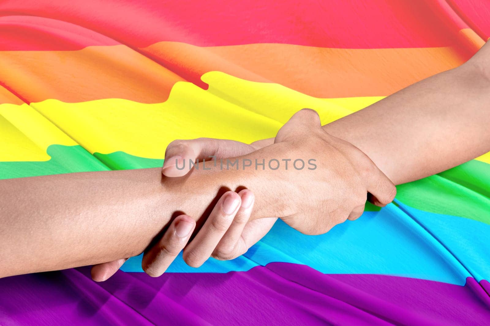 Two gay couple hands holding each other by the wrists with rainbow flag background. LGBT concept