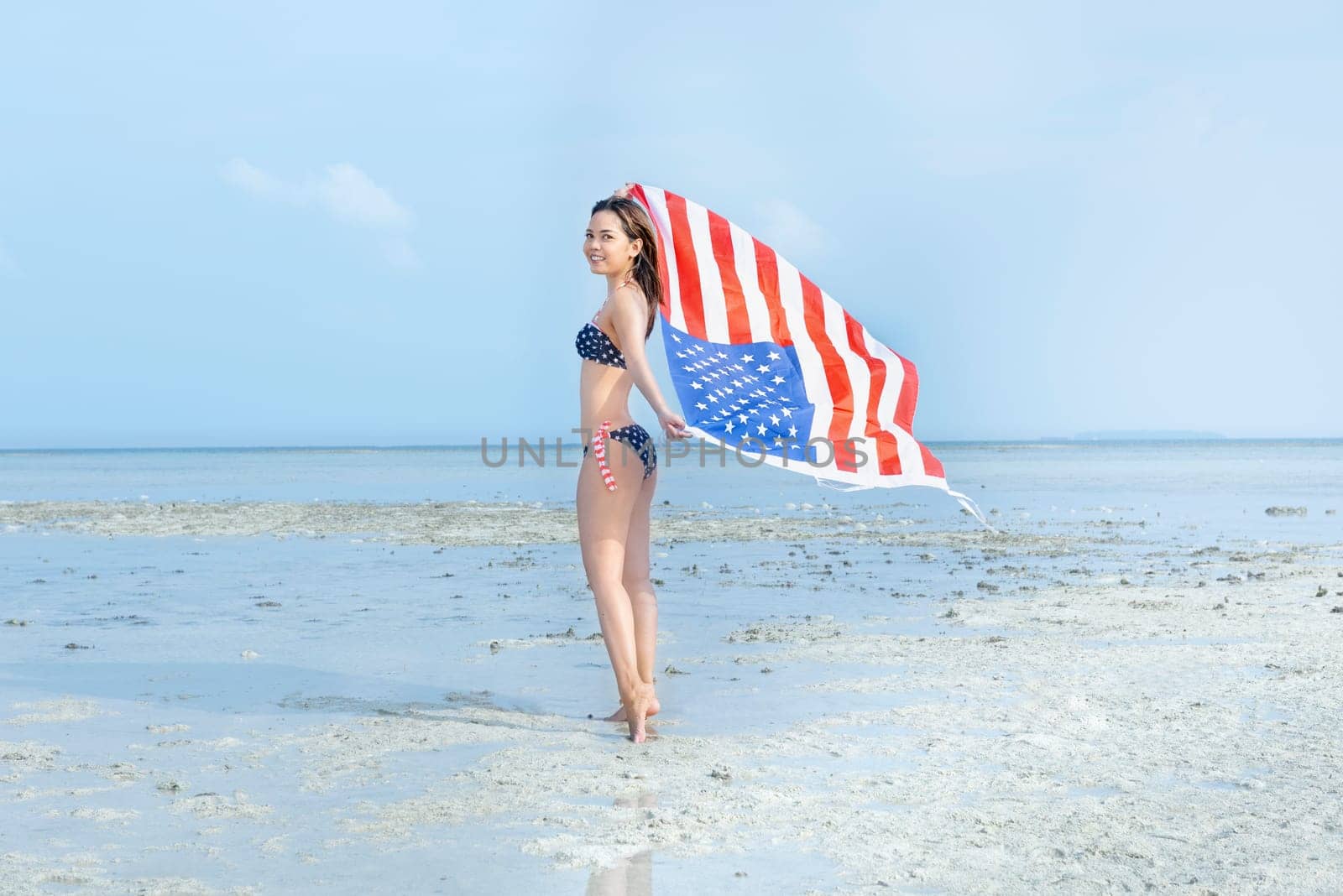 Asian sexy girl in bikini of american flag holding a waving american flag on the beach. 4th of July Independence day concept