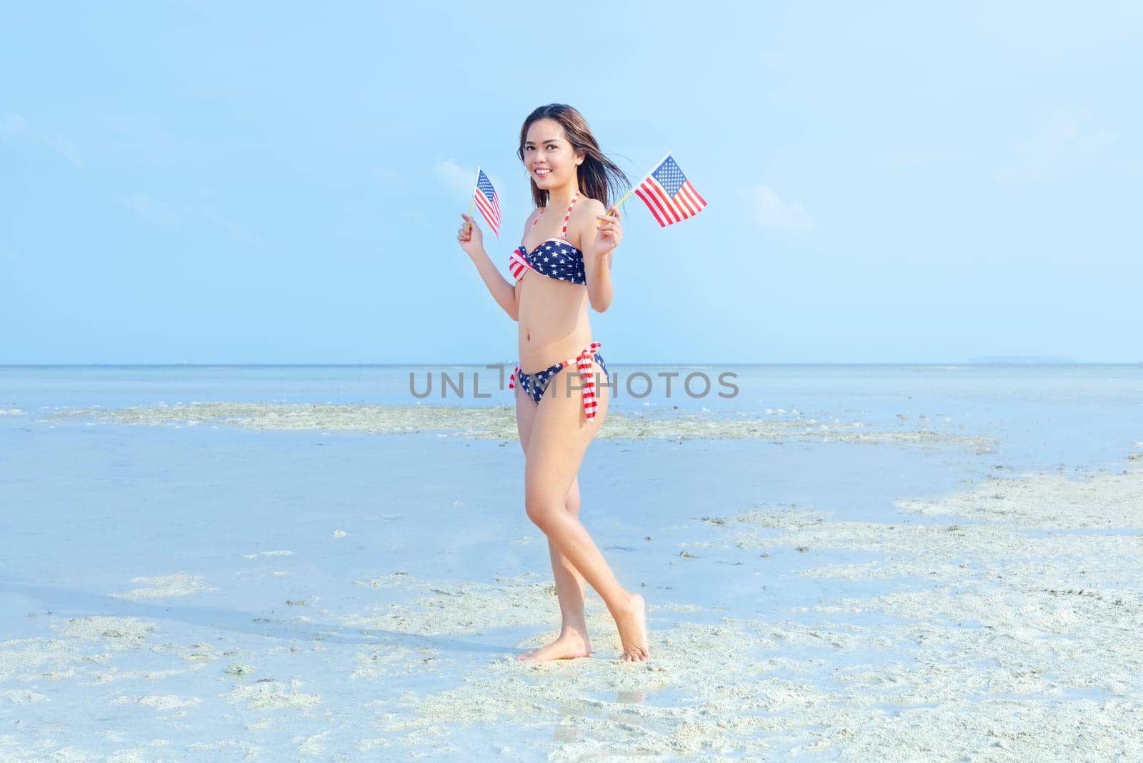 Asian sexy girl in bikini of american flag holding a little american flag on her hands on the beach. 4th of July Independence day concept