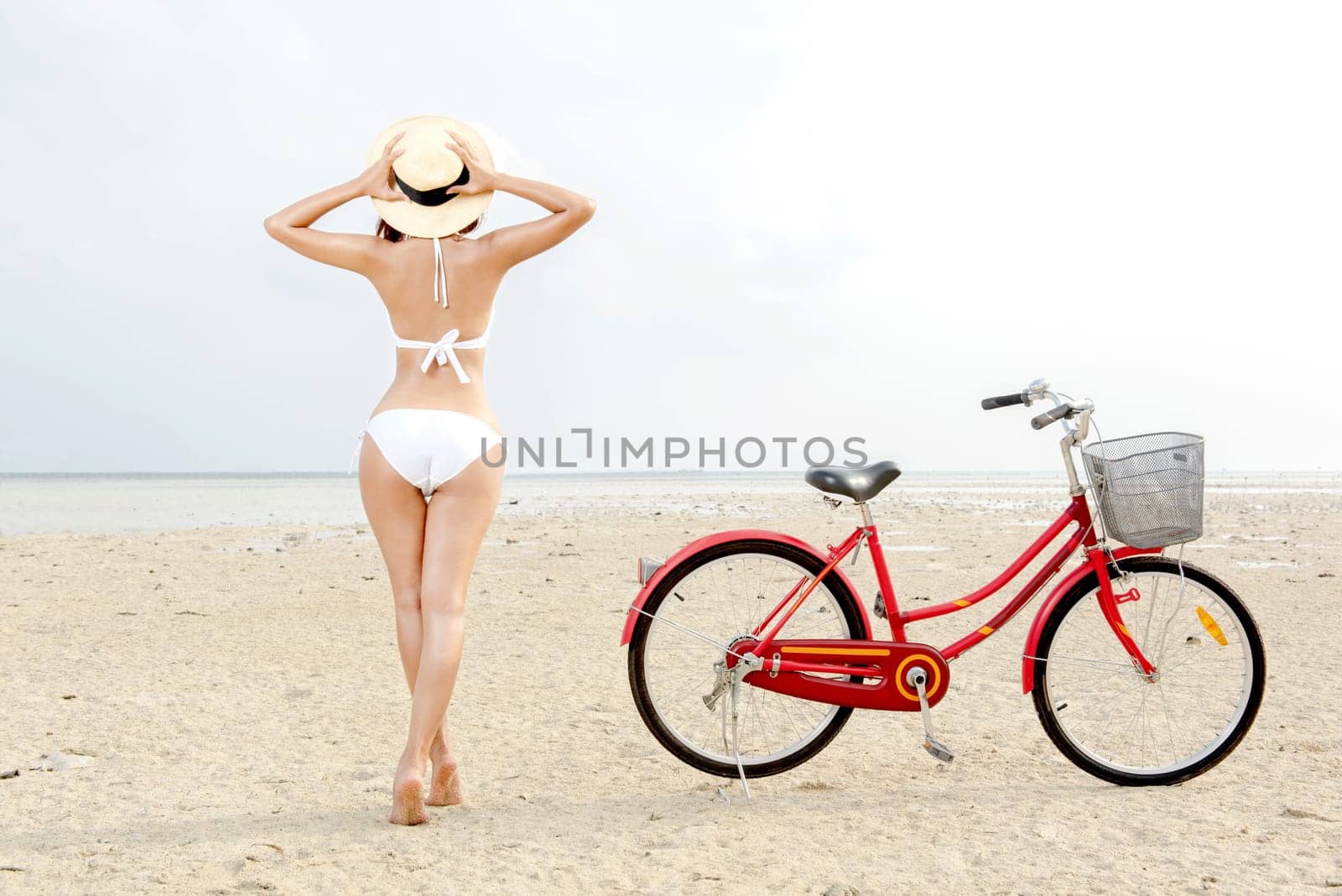 Rear view of asian sexy girl with hat and bikini with bike on the beach. Summer vacation