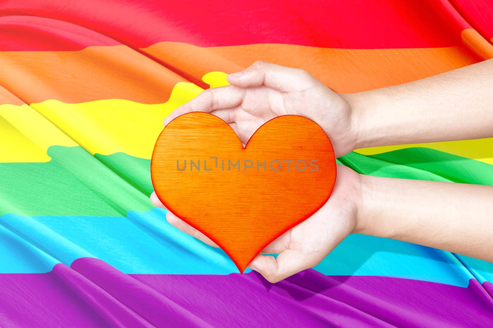 Human hands holding heart with rainbow flag background. LGBT concept