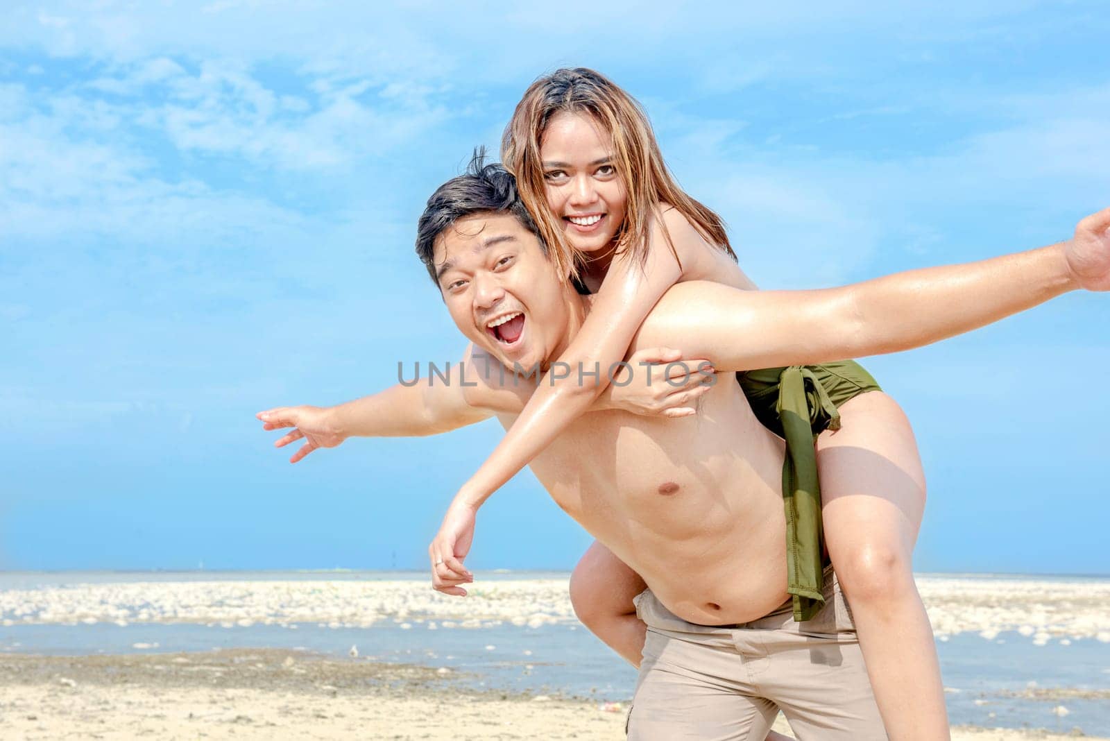 Happy asian man carrying a girl on his back in the beach. Summer vacation