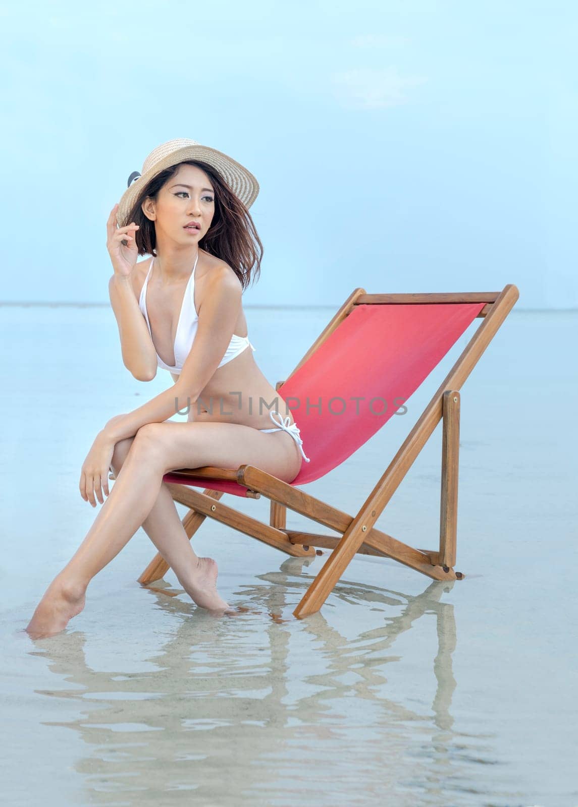 Asian sexy girl with hat and bikini sitting on the beach chair at seaside. Summer vacation